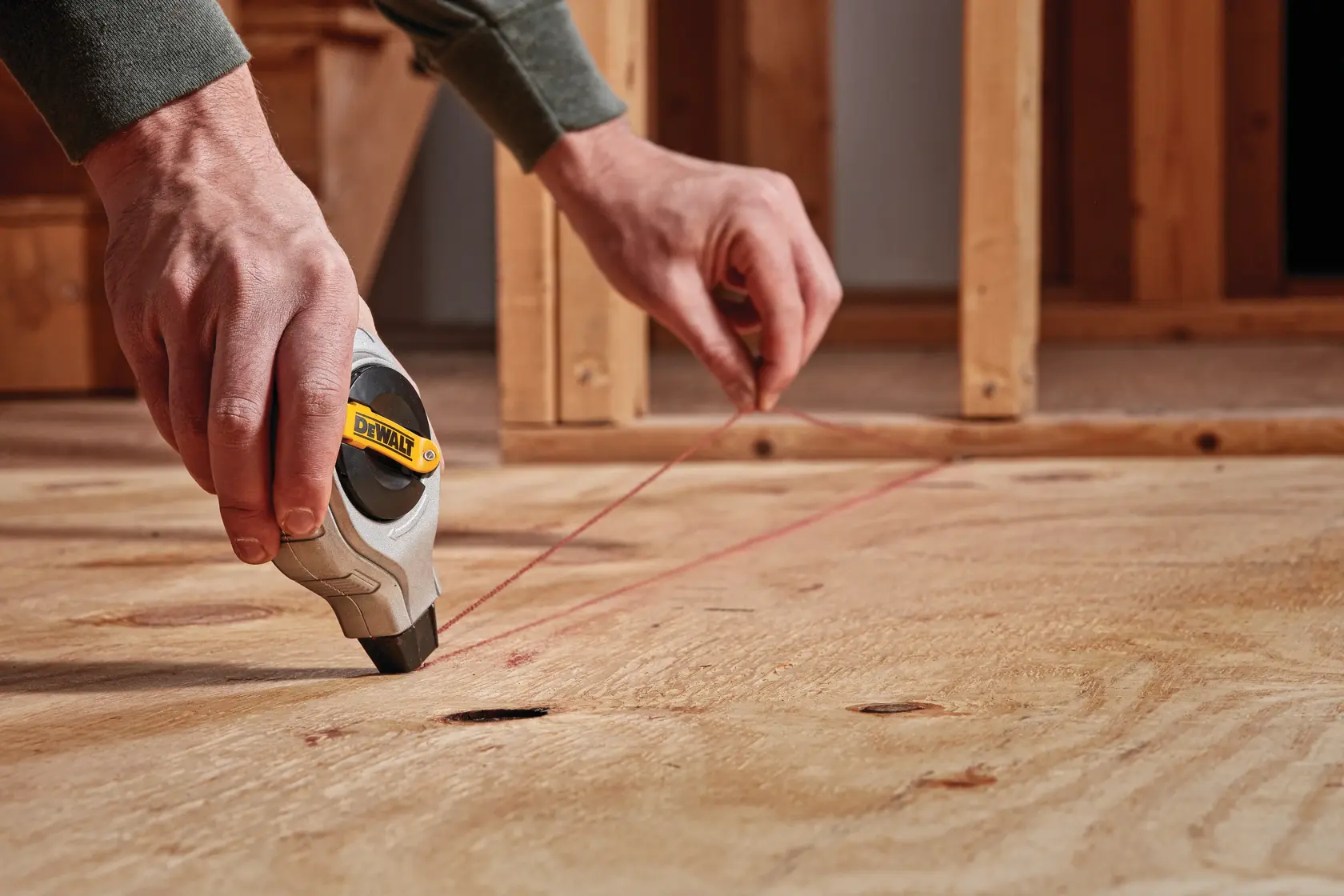 Pessoa usa ferramenta de linha de giz DEWALT no chão de madeira.