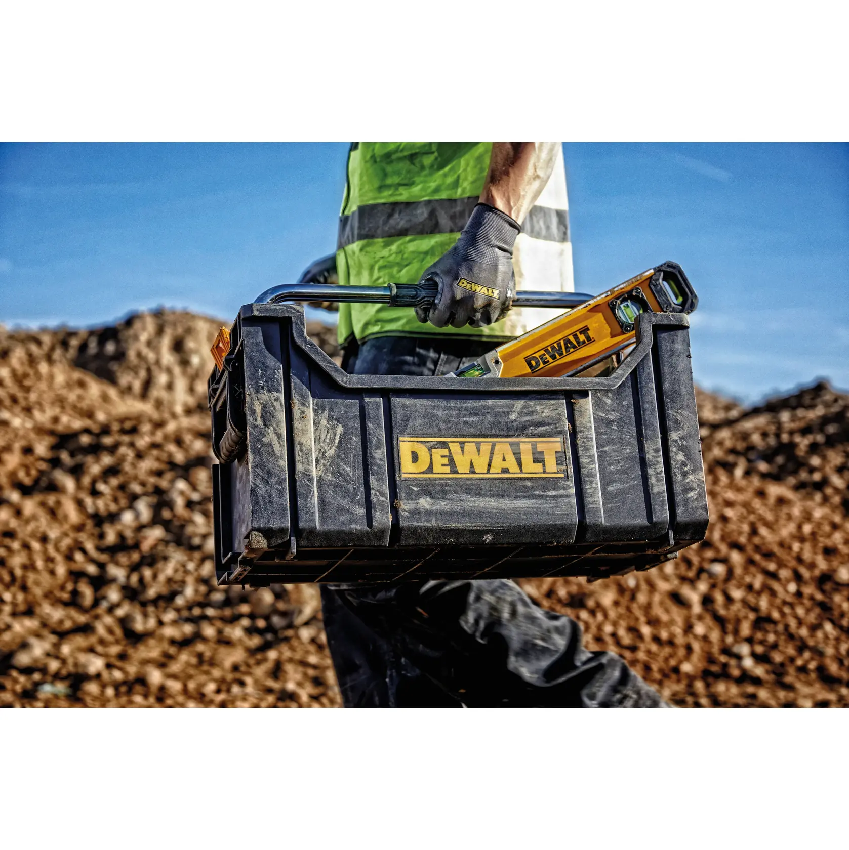 Trabalhador carregando uma caixa de ferramentas DEWALT com ferramentas na obra.