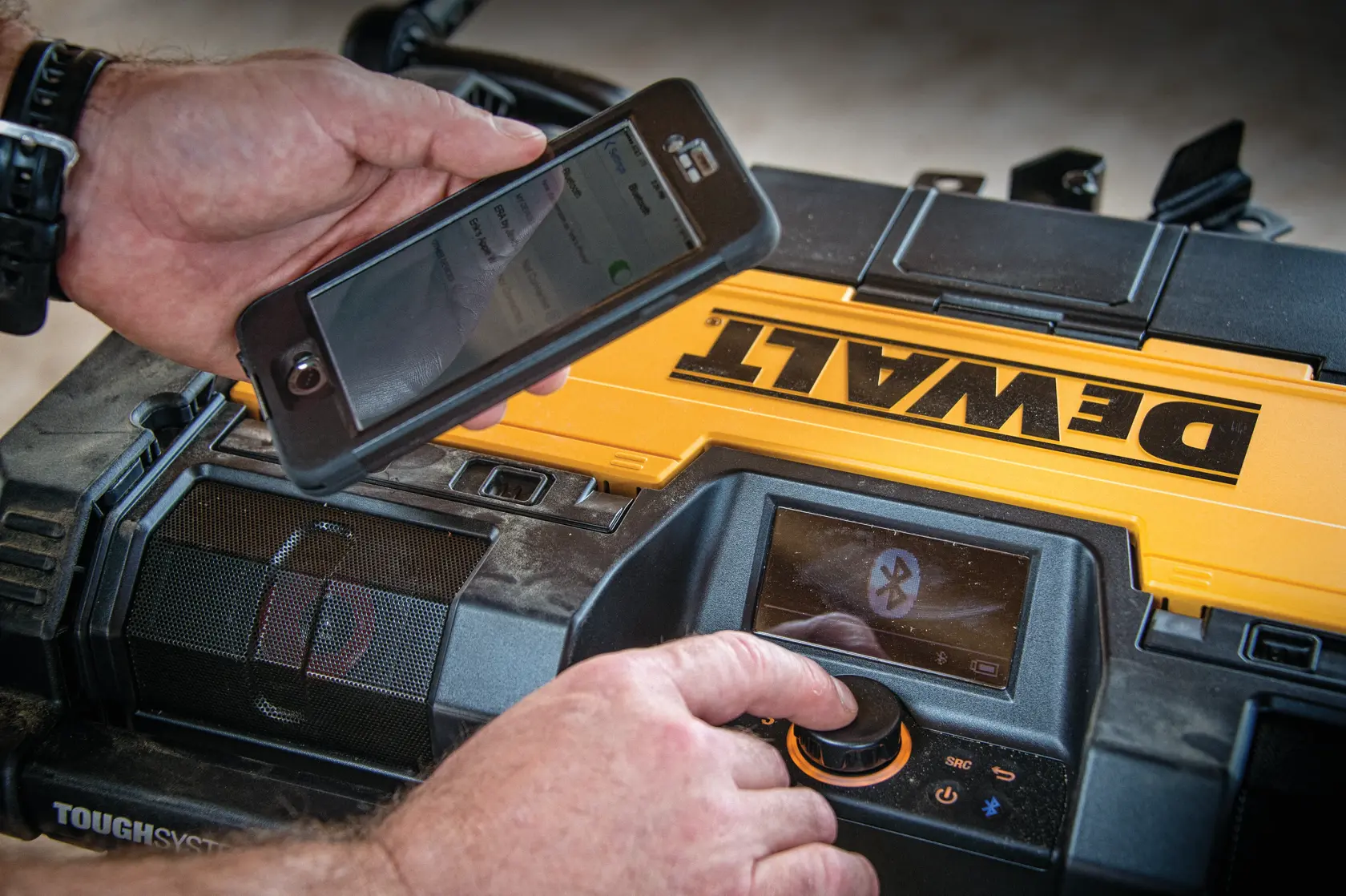 Pessoa conecta smartphone ao DEWALT ToughSystem via Bluetooth usando dial e aplicativo.
