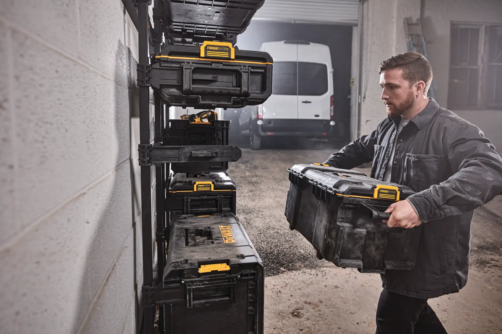 Pessoa organiza uma caixa de ferramentas DEWALT em um suporte de parede na garagem com caixas empilhadas.