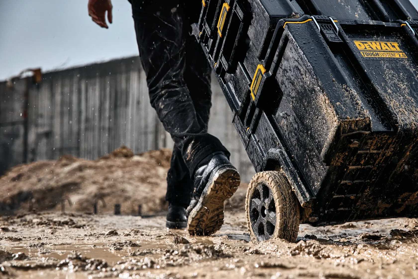Caja DEWALT ToughSystem 2.0 con ruedas siendo arrastrada en obra mojada y fangosa.