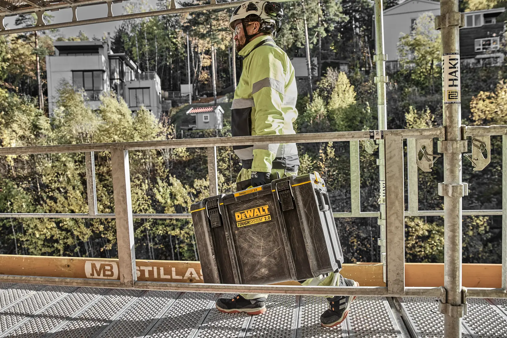 Pessoa com equipamento de segurança leva uma caixa DEWALT Toughsystem 2.0 em obra.