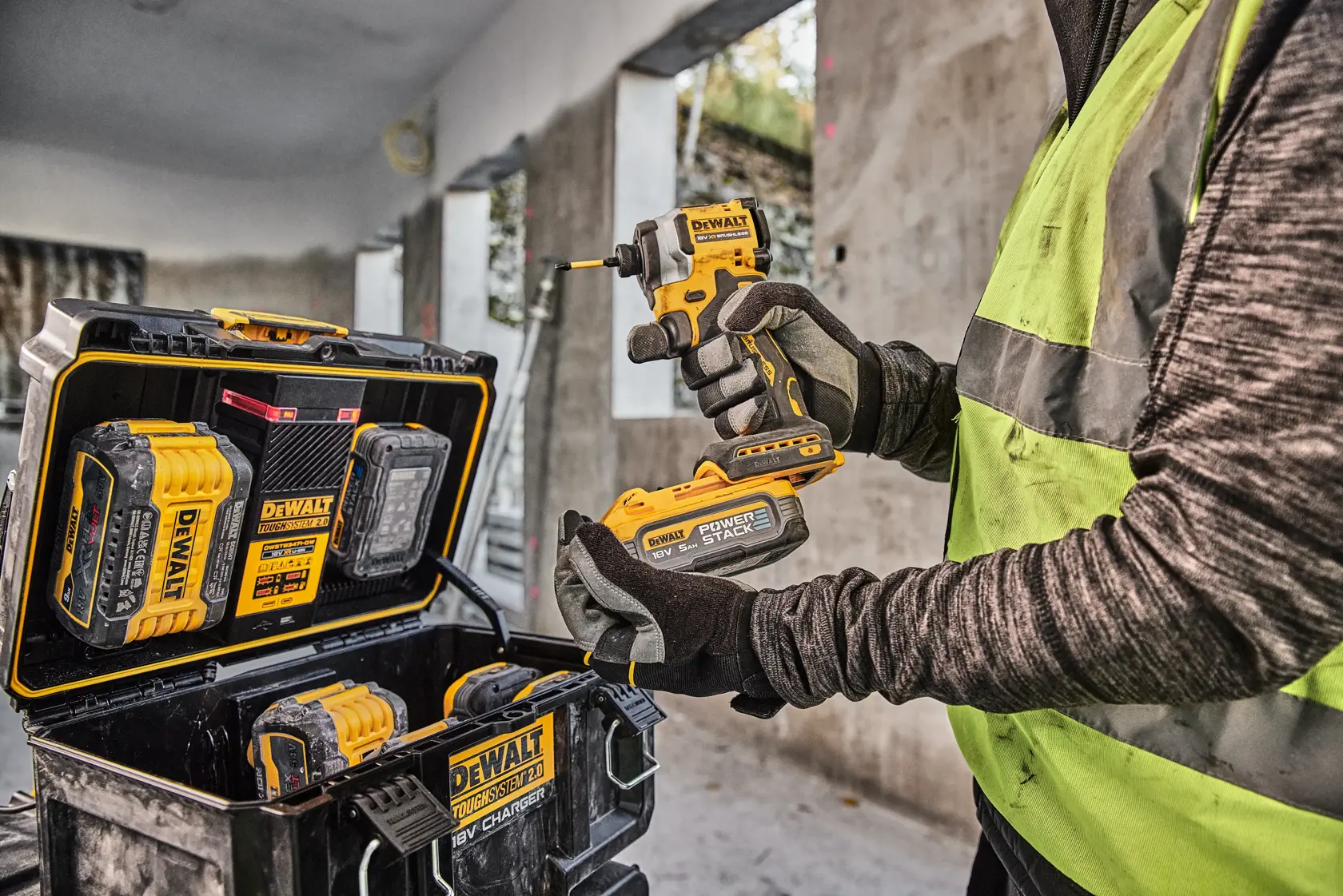 Pessoa com ferramenta DEWALT e bateria, estojo e baterias DEWALT visíveis em obra.