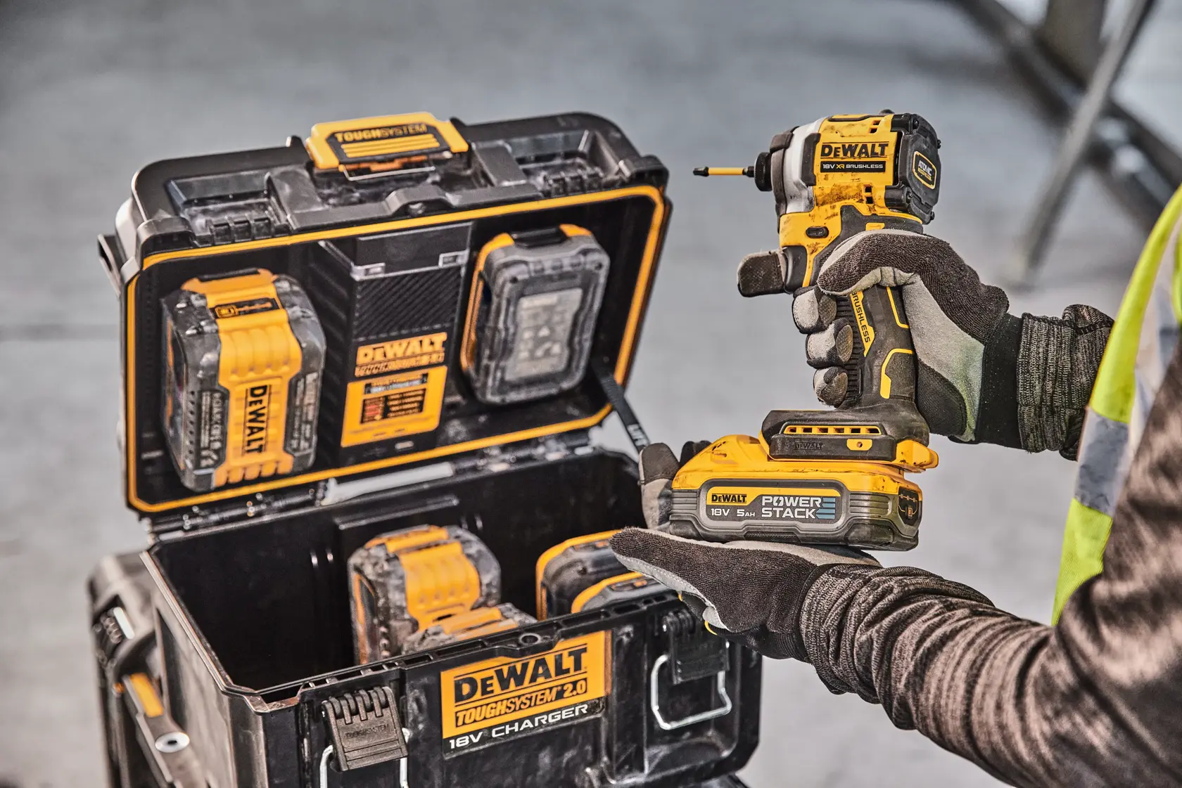 Pessoa com furadeira DEWALT, estojo de carregamento com baterias e ferramentas. Ambiente industrial.