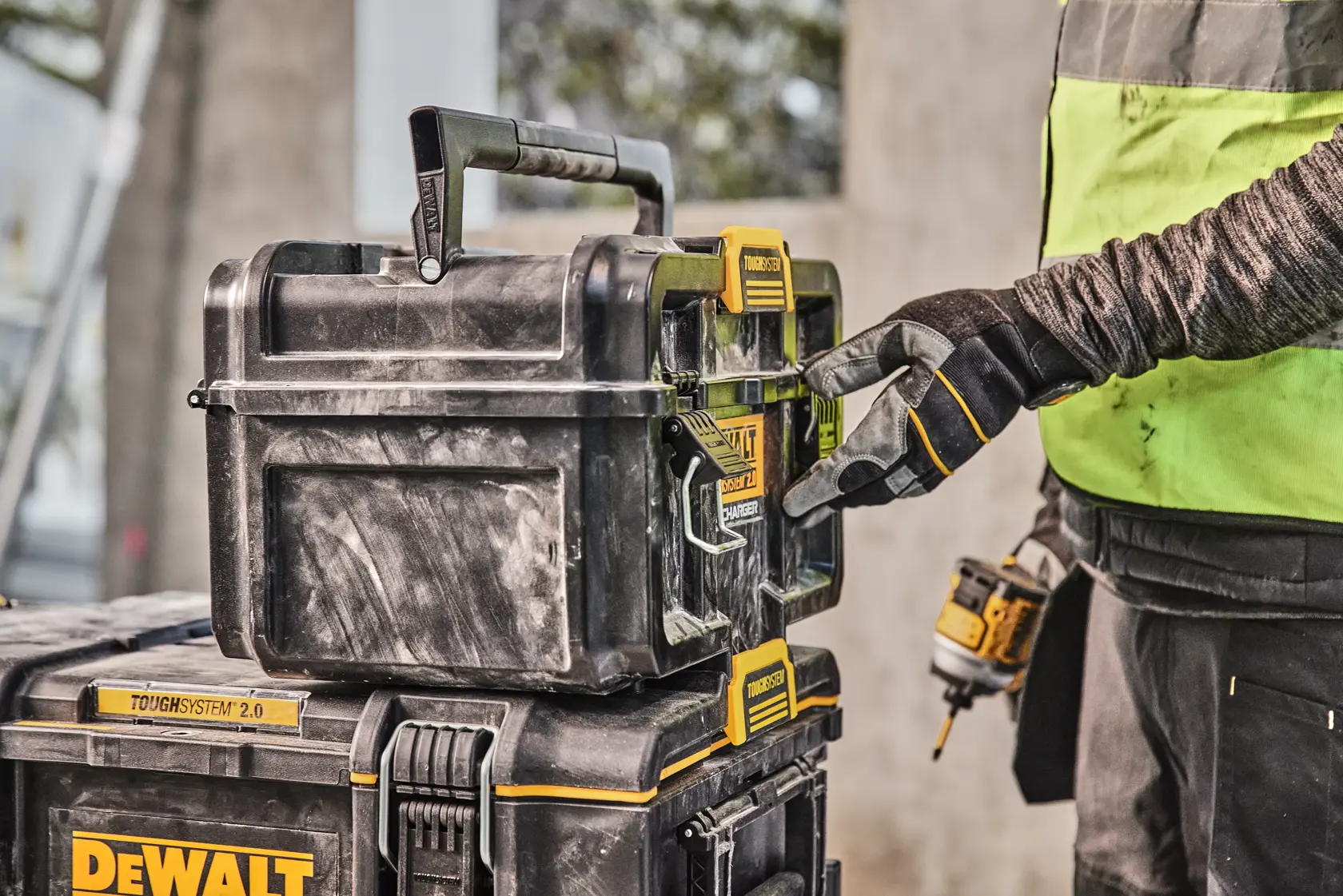 Mão com luva abre caixa de ferramentas DEWALT Toughsystem 2.0 empilhada no local de trabalho.
